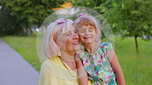 Little granddaughter child embracing kissing with her grandmother in park, happy family relationship