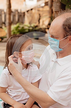 Little granddaughter in a face mask hugs and wants to protect grandfather from an epidemic