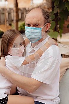 Little granddaughter in a face mask hugs and wants to protect grandfather from an epidemic