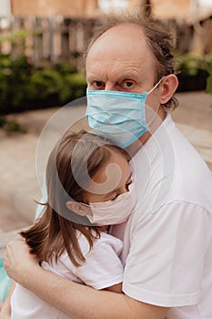 Little granddaughter in a face mask hugs and wants to protect grandfather from an epidemic