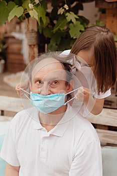 Little granddaughter in a face mask hugs and wants to protect grandfather from an epidemic