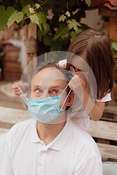 Little granddaughter in a face mask hugs and wants to protect grandfather from an epidemic