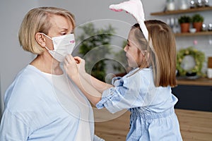 Little granddaughter helps her grandmother put on a protective mask