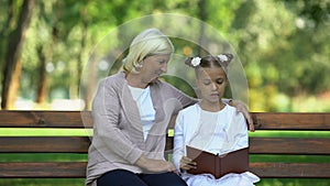 Little granddaughter reading book aloud to her grandmother, pastime in park