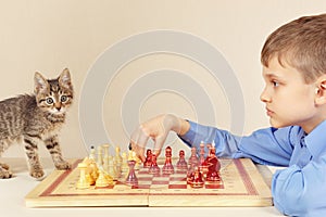Little grandmaster with kitten plays chess.