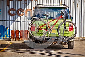 Little green car with red bike on rack parked by metal building - rear view - Colorfu