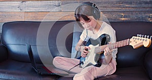 Little guitarist during an online lesson. 10 year old girl with an electric guitar sits at home in front of a laptop.