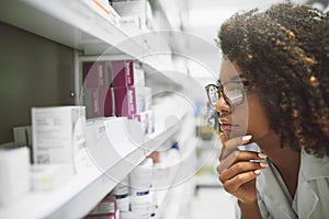 This little guy seems to be lost. Shot of a focused young female pharmacist looking closely at medication on a shelf