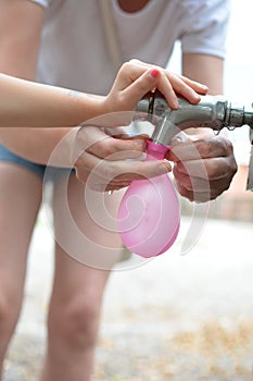 LITTLE HAND OF A GIRLD AND HER MOTHER FILLING A PINK WATER BALL