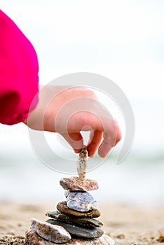 Little Hand placing Stone on the Pyramid on sand. Sea in the bac