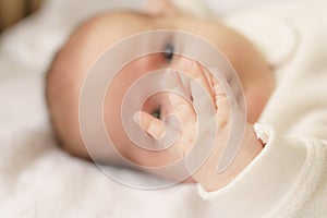 Little hands of newborn.Newborn baby in a white bodysuit lying on the bed. Top view of a newborn baby on a white warm