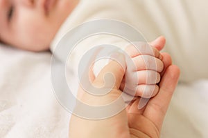 Little hands of newborn. Little newborn baby in a white bodysuit lying on the bed. Top view of a newborn baby on a white