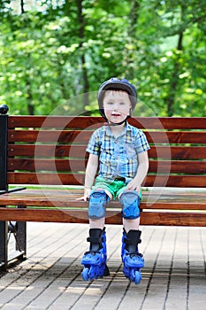 Little handsome boy in roller-blades sits on bench