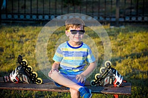 Little handsome boy in roller-blades sits in bench in summer par