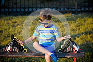 Little handsome boy in roller-blades sits in bench in summer par