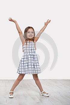 A little happiness girl with long blonde hair raised her hands up rejoicing at something on a white background in studio