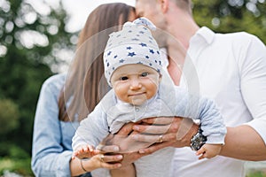 Little happy baby in the arms of loving parents in the summer in the park