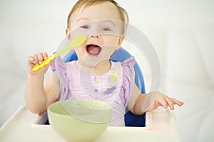 Little happy baby with spoon sits at highchair and