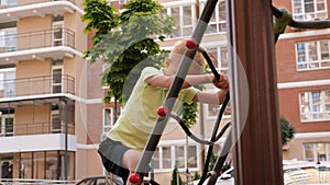 A little happy boy climbs a rope ladder on a playground in the yard.