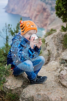 Little happy boy is drinking from a thermos