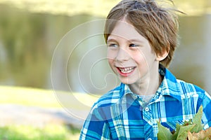 Little happy boy with fall leaves over sunny nature background,