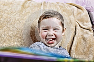 Little happy boy laughing hile sitting on the couch. close up