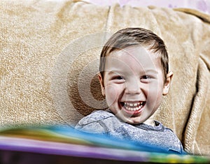 Little happy boy laughing while sitting on the couch . close up