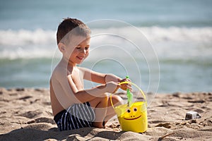 Little happy boy play with sand and toys on summer beach