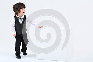 Little happy boy stands near large cube and laughs on white back photo