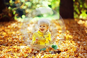 Little happy boy in yellow jacket playing with leaves