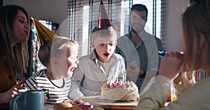 Little happy Caucasian boy child making wish, blow on birthday cake at surprise family party with confetti slow motion.