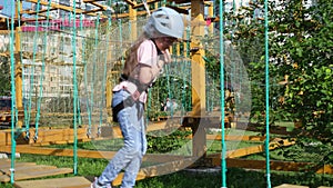 A little happy Caucasian girl is a child in an adventure park in protective gear on a summer day. Rope park. nature