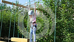 A little happy Caucasian girl is a child in an adventure park in protective gear on a summer day. Rope park. nature