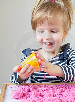 Little Happy Caucasian Girl Playing with Pink Kinetic Sand at Home