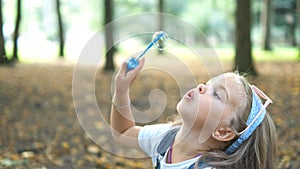 Little happy child girl blowing soap bubbles outdoors in summer park