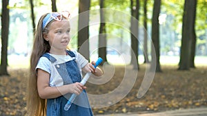 Little happy child girl blowing soap bubbles outdoors in summer park