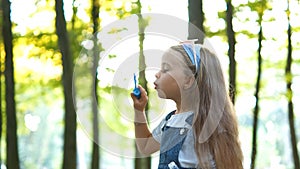 Little happy child girl blowing soap bubbles outdoors in summer park