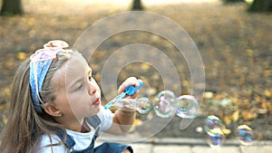 Little happy child girl blowing soap bubbles outside in green park. Outdoor summer activities concept