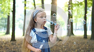 Little happy child girl blowing soap bubbles outside in green park. Outdoor summer activities concept