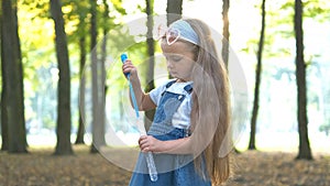Little happy child girl blowing soap bubbles outside in green park. Outdoor summer activities concept