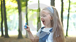 Little happy child girl blowing soap bubbles outside in green park. Outdoor summer activities concept