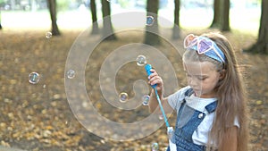 Little happy child girl blowing soap bubbles outside in green park. Outdoor summer activities concept