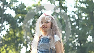 Little happy child girl cathing and bursting soap bubbles outdoors in summer.