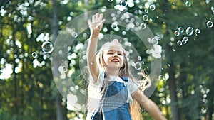Little happy child girl cathing and bursting soap bubbles outdoors in summer