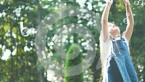 Little happy child girl cathing and bursting soap bubbles outdoors in summer.