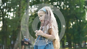 Little happy child girl jumping up and chasing soap bubbles outdoors in summer park