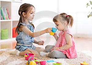 Little happy children, cute toddler and kid girls play with plastic toy kitchen on floor at home or kindergarten