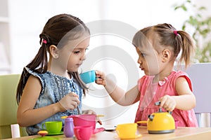 Little happy children, cute toddler and kid girls play with plastic toy kitchen indoors at home or kindergarten