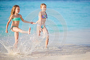 Two little happy girls have a lot of fun at tropical beach playing together at shallow water.