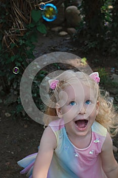 Little happy funny girl with blond hair catching soap bubbles in amusement park
